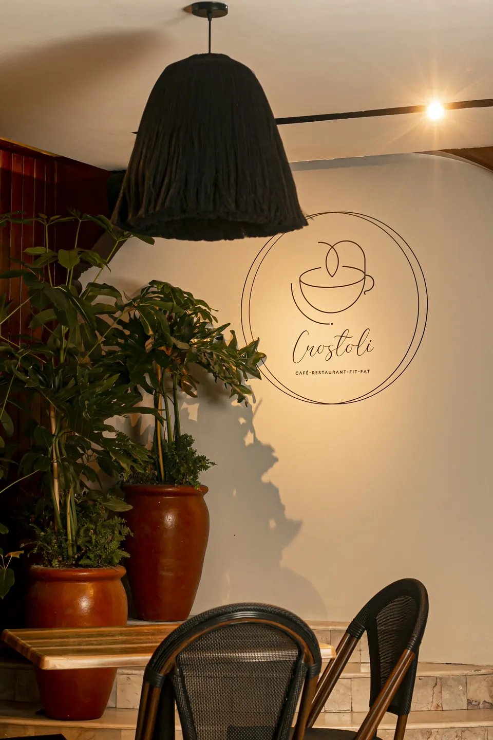 Logo de Crostoli en el muro, junto a plantas y una lámpara tejida